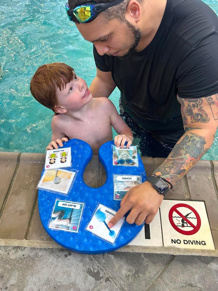 An instructor and a young swimmer working through a visual schedule board at the pool edge